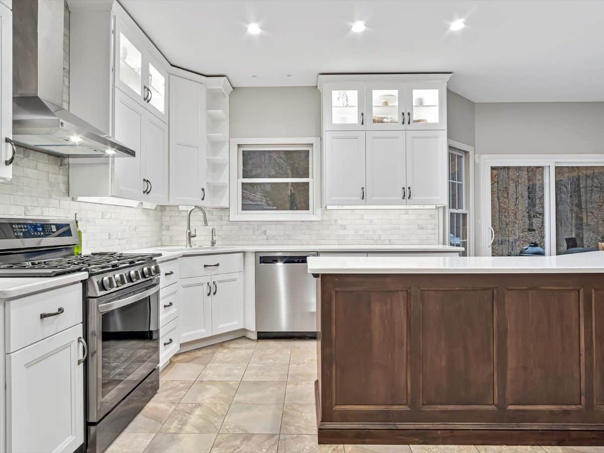 Kitchen remodel in Eureka, MO showing custom stacked wall cabinets with glass doors at the top painted white, a dark stained island and travertine tile flooring.