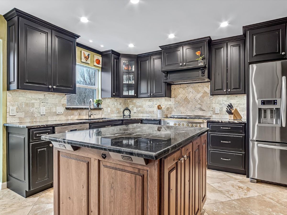 Rustic Imperial kitchen remodel showing distressed and glazed stained island with black custom cabinets with rub through all with black granite countertops.