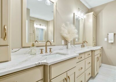 Double sink vanity in off-white paint with glaze. Quartz countertops, framed mirrors and gold widespread faucets.