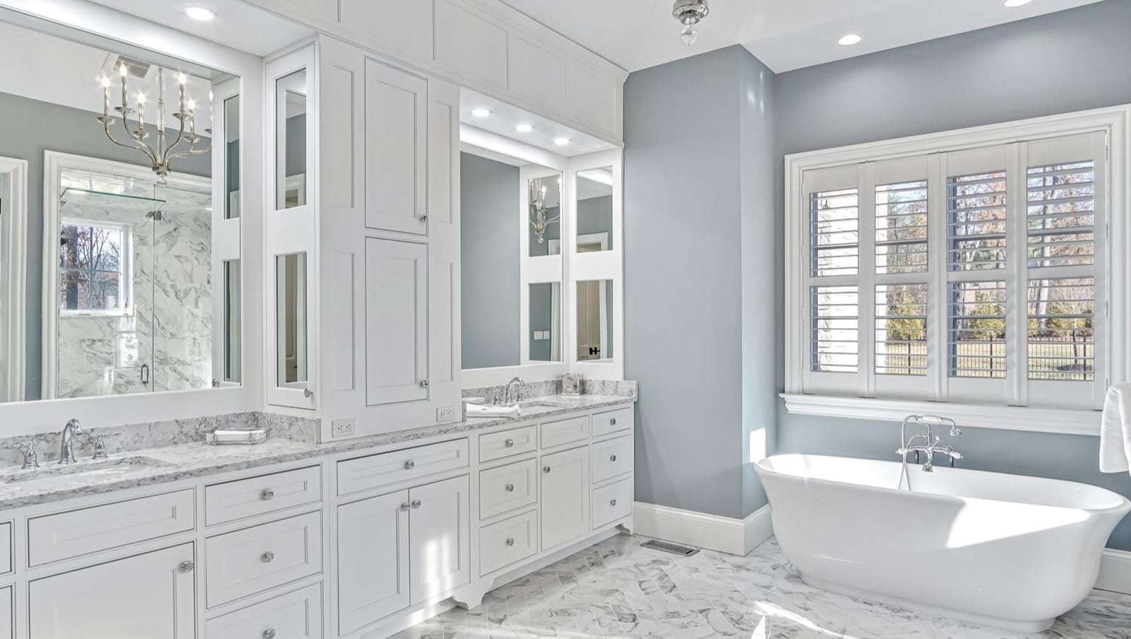 Custom master bathroom vanity in white finish with framed mirrors and custom upper cabinet.  Freestanding tub sits below window perpendicular to the vanity.
