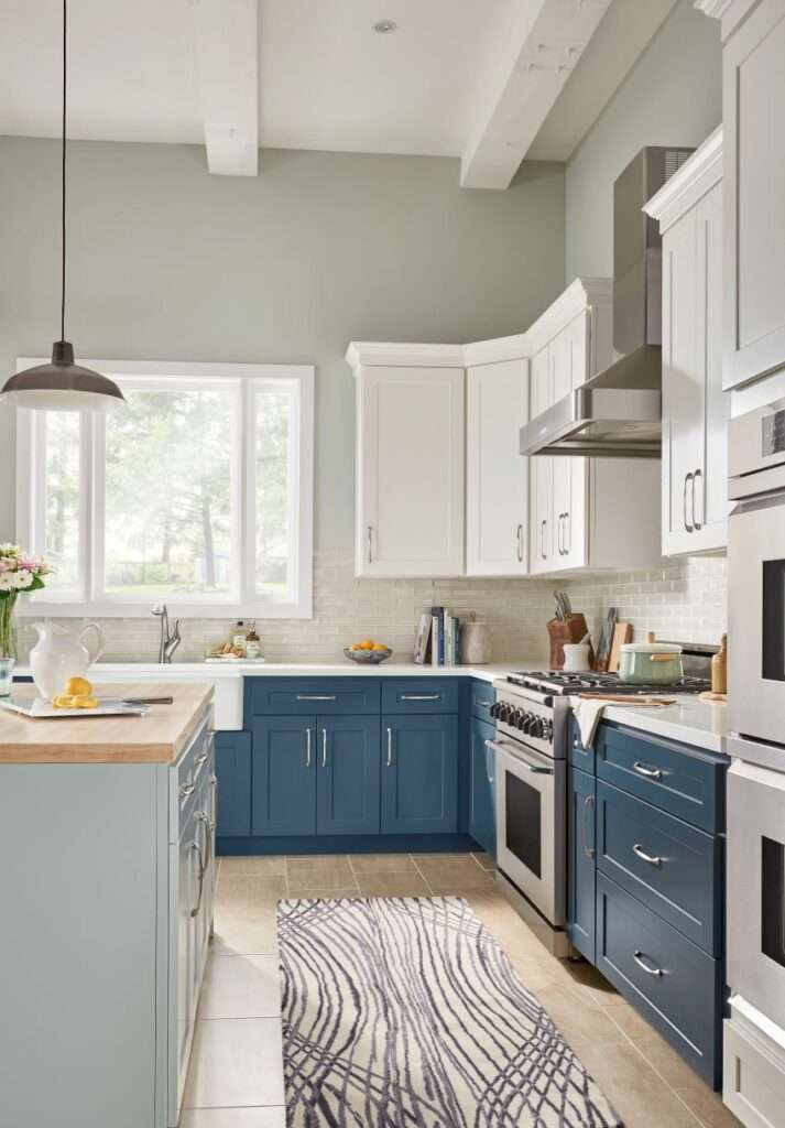 Kitchen view facing farm sink below window. Kitchen features white painted wall cabinets, blue base cabinets on the perimeter and gray cabinets for the island. White quartz tops on perimeter with natural wood for island countertop.