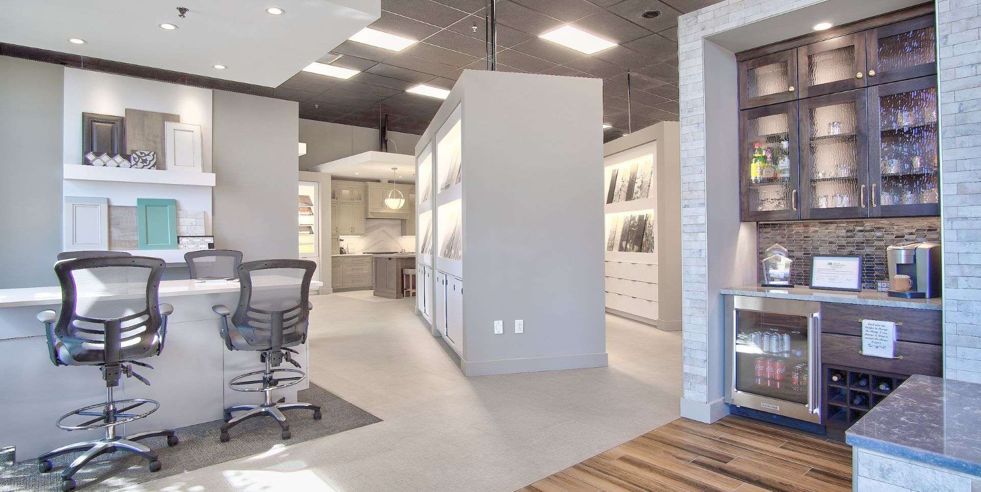 Entrance of the Thompson Price Kitchen and Bathroom Design Center in St Louis, MO. Lay table on left, large white tile display areas in middle, coffee bar with stained cabinetry to the right.