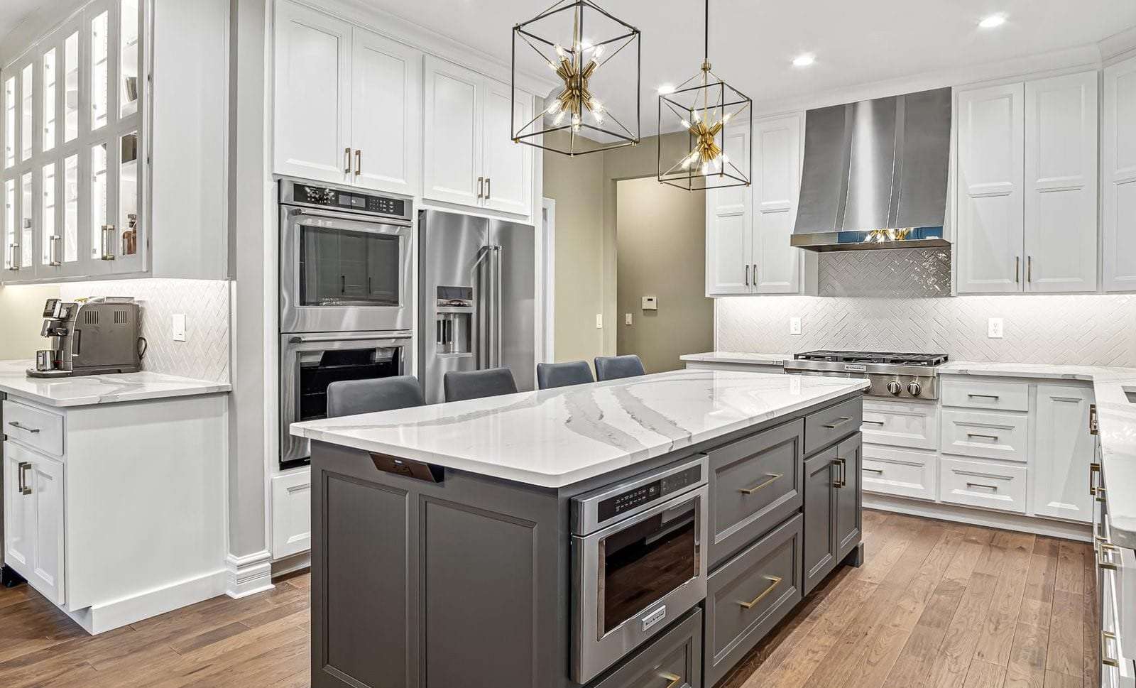 kitchen remodel is st louis with white perimeter cabinets and dark gray island cabinets with large stainless steel hood with polished accents.