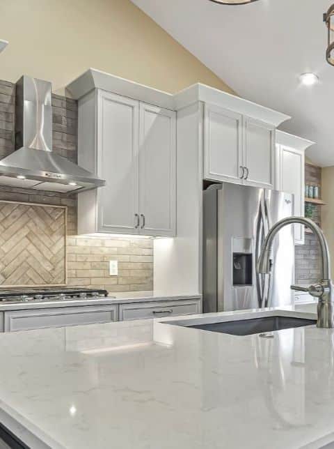 White kitchen cabinets with neutral backsplash tiles with diagonal pattern with border over cooking area and stainless steel hood.