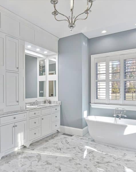 Master bathroom remodel with large inset white vanity on left and freestanding traditional tub on right sitting below window