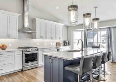 Kitchen remodel showing white Waypoint cabinets on the wall and custom gray painted island cabinetry. Subway tile backsplash and stainless steel hood.