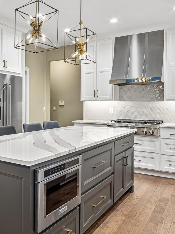 Kitchen remodel in St Louis featuring white custom cabinets around perimeter of room and a large island with dark gray cabinets all with white quartz with gray veining.