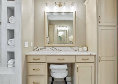 Thompson Price custom master bathroom with tan painted cabinets showing sit down makeup area and custom towel storage at shower area