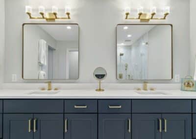 Custom blue vanity cabinet with double sink and brass mirrors with brass lighting above. Custom remodeled bathroom in St Louis, MO.