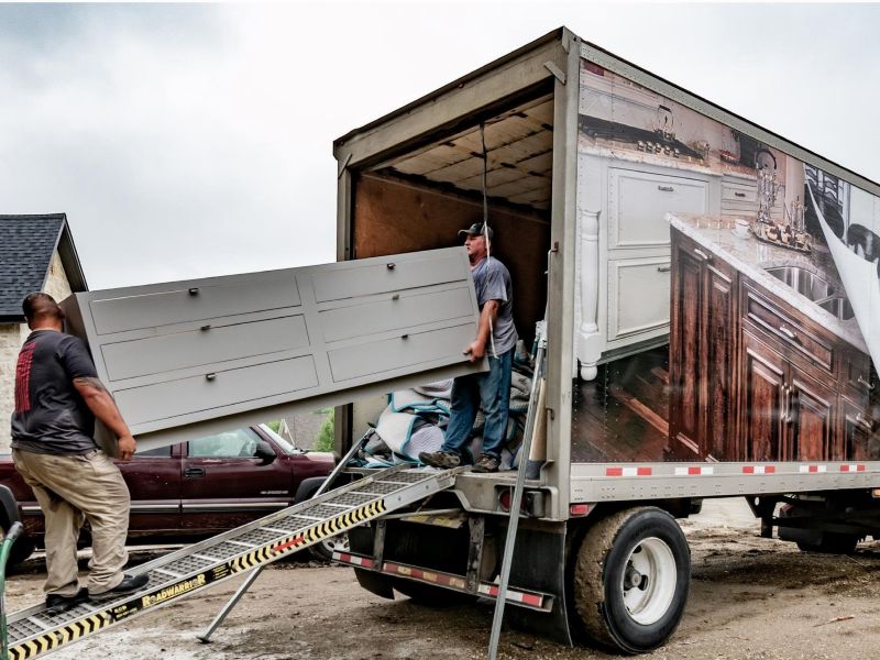 View of one of custom kitchen cabinets being delivered to the jobsite with two men carrying the cabinet off the delivery truck.