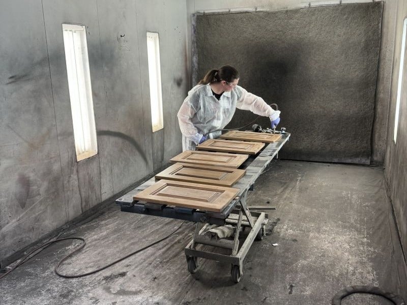 Custom cabinet doors getting hand-finished in a spray booth by one of our artisans