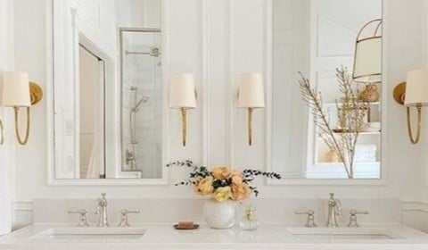 View of wall behind bathroom vanity with brass sconce lights installed on each side of bathroom mirror