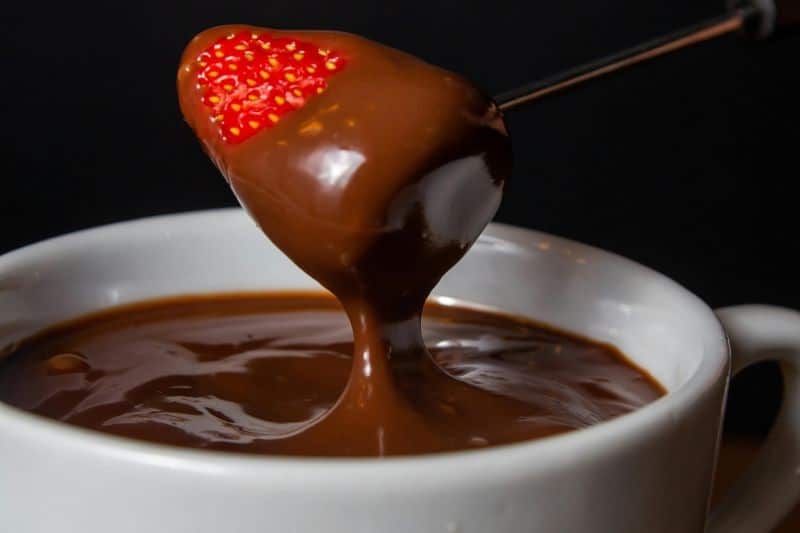 An awesome strawberry being dipped in warm melted chocolate