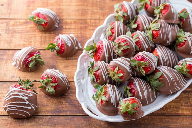 Chocolate covered strawberries laid out on a wood countertop with decorative touches