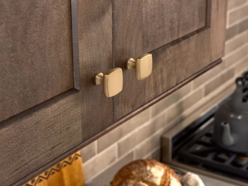 Square kitchen cabinet knobs in brushed satin finish against dark stained cabinet doors