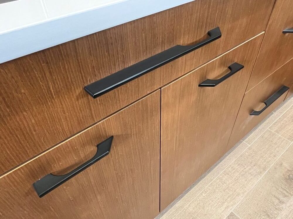 Thompson Price asymmetrical kitchen cabinet hardware with black tapered pulls in matte black finish installed on cherry veneer cabinets